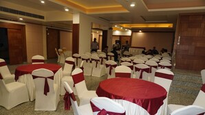 A conference room with round tables and white chairs with red sashes, arranged for a meeting or event. - Hotel Nilax (Jaipur)