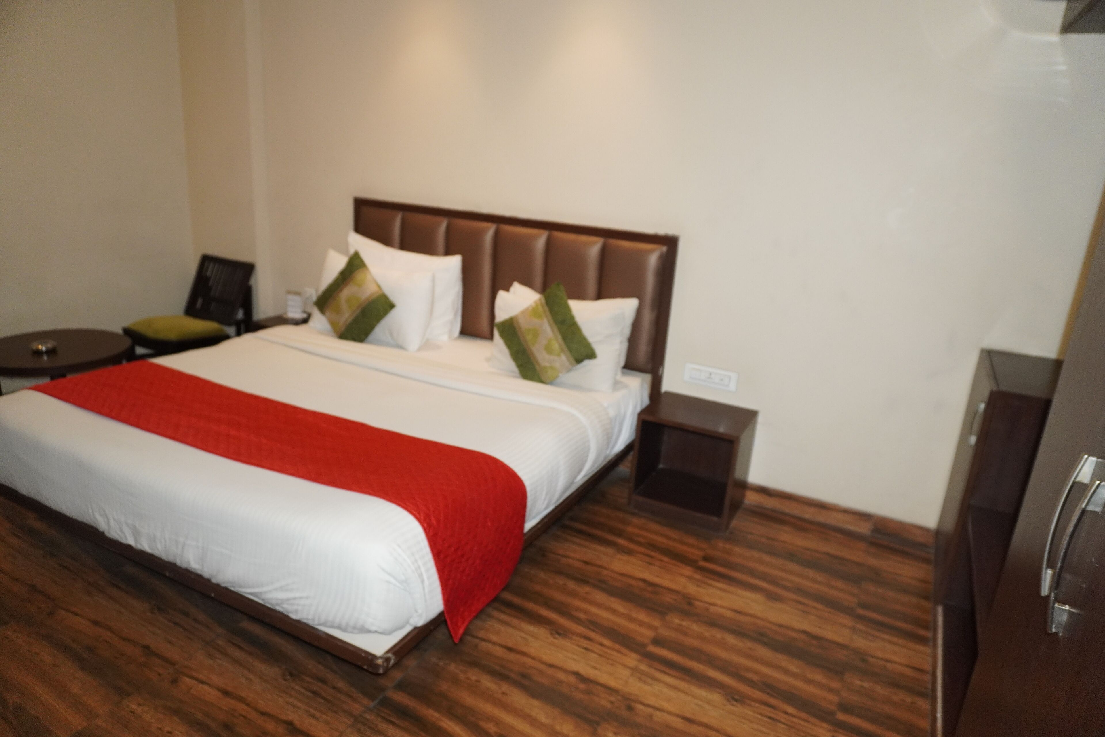 A hotel room with a large bed, wooden flooring, a nightstand, and a dresser.