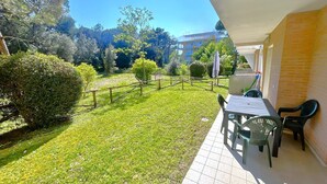 Un balcón con una mesa y sillas, un jardín con césped y vistas a árboles y edificios.