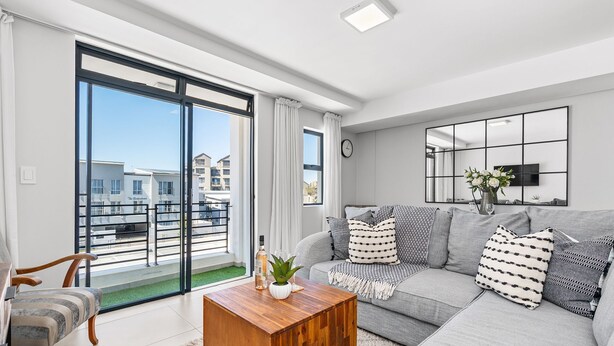 A modern living room with a grey sofa, a wooden coffee table, and a large window offering a view of buildings. - Beach Break 17 (Cape Town)