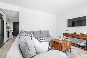 Un soggiorno moderno con un divano grigio, un tavolino in legno e una TV a parete.