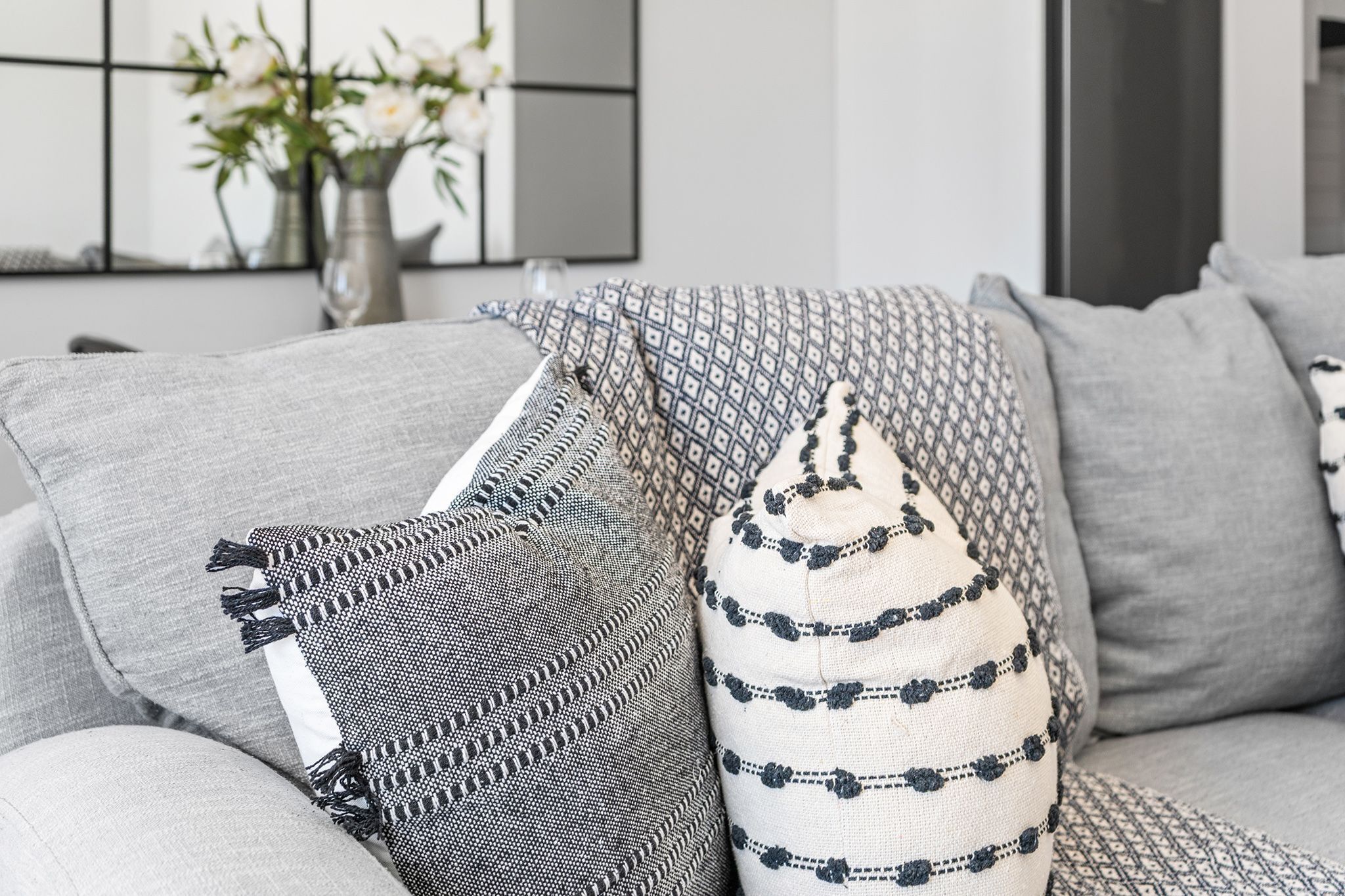 A grey sofa with patterned cushions and a vase with flowers in the background.