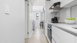 A modern kitchen with white cabinetry, a black stove, and a bowl of green apples on the counter. - Beach Break 17 (Cape Town)