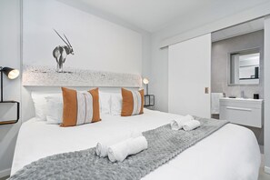 Una moderna camera d'albergo con un letto grande, una testiera con una stampa di fauna selvatica, un comodino, uno specchio e un bagno con lavandino e specchio.