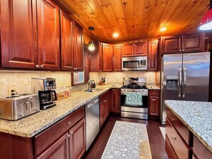 A kitchen with wooden cabinets, stainless steel appliances, granite countertops, and a wooden ceiling. - Private, Comfy Cabin in Rangeley/Trails, Lakes, Fire Pit/Sleeps 8/Starry Sky (Rangeley)
