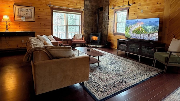 L’intérieur d’un chalet confortable, avec une cheminée, des fauteuils confortables et un téléviseur.
