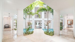 Un lobby amplio con piscina central, pilares blancos y palmeras.