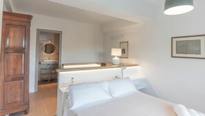 Quarto com cama, guarda-roupa de madeira, banheiro com pia e espelho, incluindo um espelho redondo.