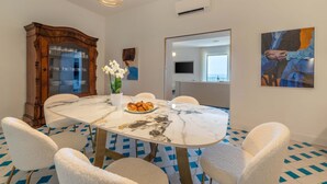 A dining area with a marble table, white chairs, a wooden cabinet, and a vase with flowers. - Maison Marika in Sorrento (Sorrento)