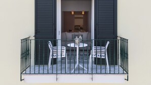 A balcony with a table and two chairs, a small table with a pitcher and glasses, and a view into a room with a sofa and a coffee table. - Maison Marika in Sorrento (Sorrento)
