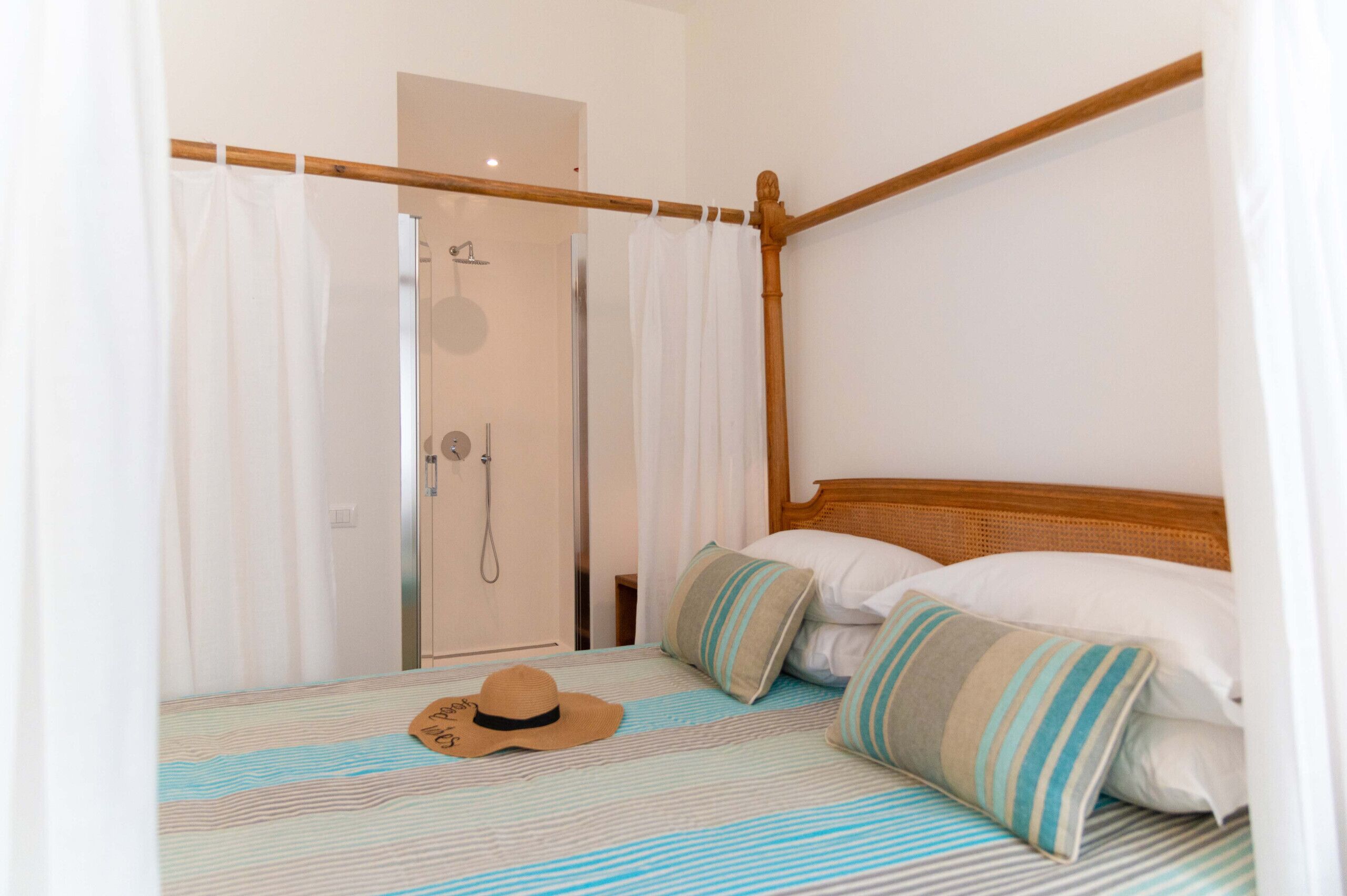 A bedroom with a wooden four-poster bed, striped bedding, and a hat on the bed.
