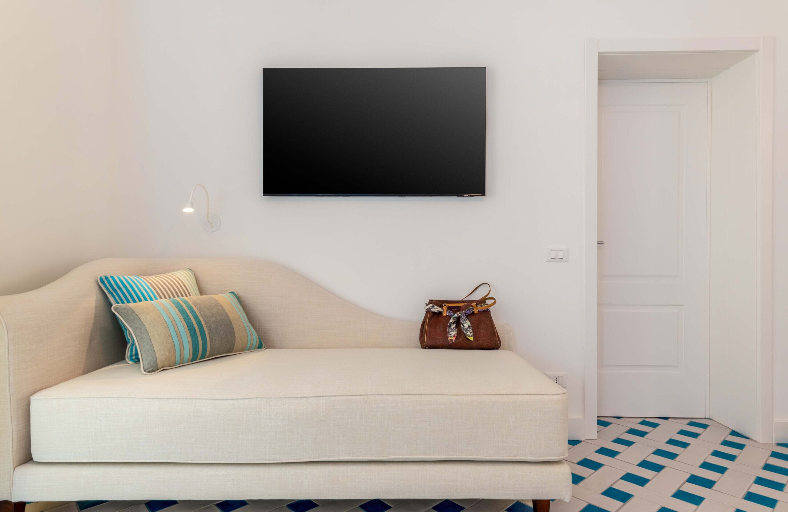 Ein Zimmer mit einer Couch, einem Wandfernseher, einer Tür und einem gemusterten Boden.