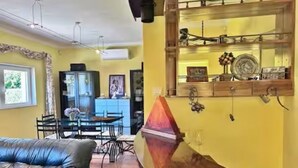A living room with a sofa, a dining table with chairs, and a wall-mounted shelf with decorative items.