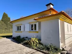 Una casa de un piso con tejado de tejas, una chimenea y un pequeño jardín con plantas.