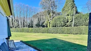 A patio area with a table and chairs, a view of a well-maintained lawn, and a hedge in the background.