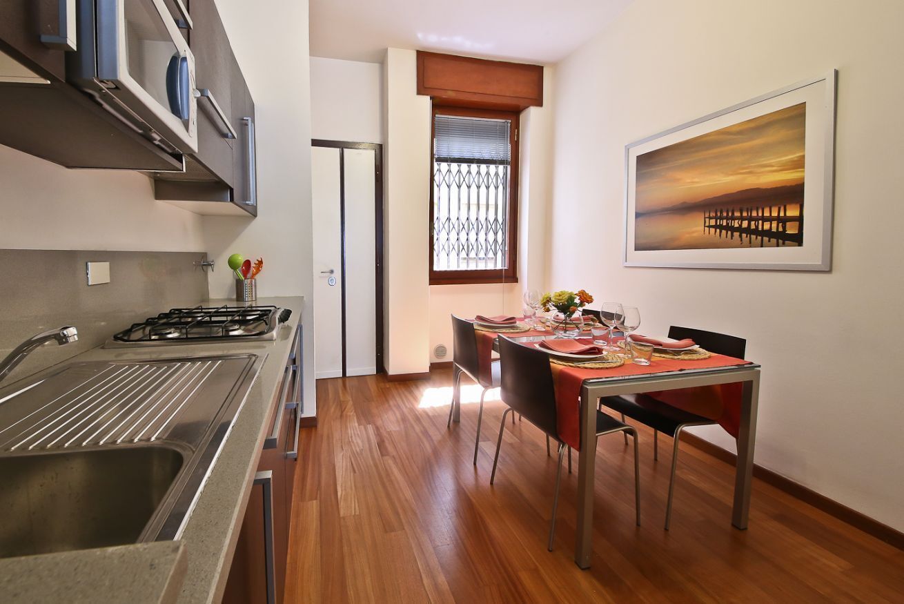 A modern kitchen with a gas stove, a sink, and a dining area with a table set for two.