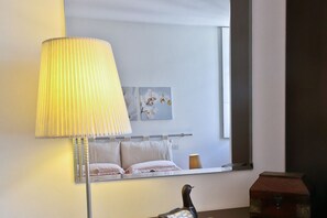 Ein Hotelzimmer mit Bett, Nachttischlampe, Spiegel und Fenster.