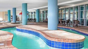 Una piscina interior con bordes de azulejos azules, rodeada de suelo de ladrillo y sostenida por pilares azules.