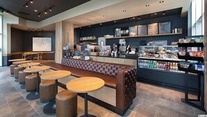 Un café moderno con una barra larga, zona de mesas y un cartel con la carta.