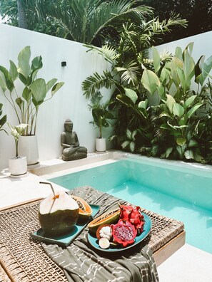 Ein Poolbereich mit Korlounge-Stuhl, einem Tisch mit Obstplatte und einer Buddha-Statue.