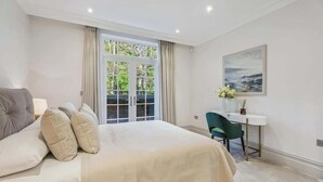 A bedroom with a large bed, a desk, and a chair. There is a window with curtains and a painting on the wall. - Luxury 2BR|Exclusive Gated Development by Tempstay (Sunningdale)