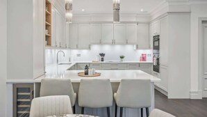 A modern kitchen with white cabinetry, a central island with bar stools, pendant lighting, and built-in appliances. - Luxury 2BR|Exclusive Gated Development by Tempstay (Sunningdale)