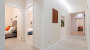 Un pasillo moderno de hotel con una paleta de colores neutros, una cama con almohadas naranjas y una obra de arte colgada en la pared.