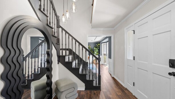 A modern staircase with a unique wavy design, a bench, and a view into a bright room with a door and a window. - Big Pool, Hot Tub & Gym at Spacious 5 Bedroom Home (Overland Park)