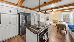 A kitchen with white cabinets, a stainless steel refrigerator, a gas stove, and a dining area with a table and chairs. - Big Pool, Hot Tub & Gym at Spacious 5 Bedroom Home (Overland Park)