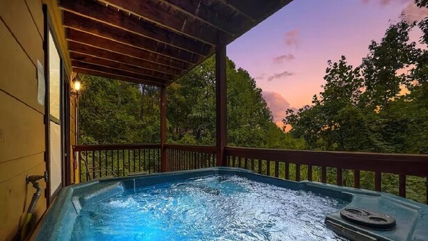 Ein Whirlpool unter einer Holzpergola mit Blick auf Bäume und einen Sonnenuntergang.