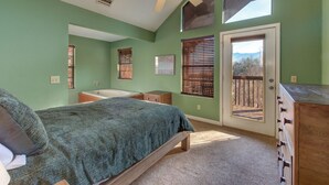 Ein Schlafzimmer mit Bett, Schminktisch, einem Fenster mit Jalousien, Deckenventilator und einer Tür, die auf einen Balkon führt.