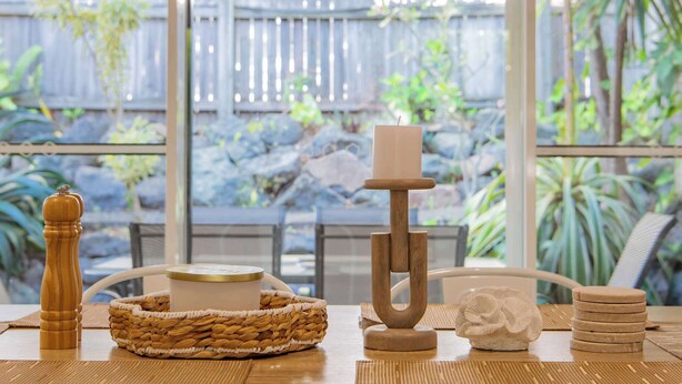 A table with a candle holder, a woven basket, a stack of coasters, and a decorative item.