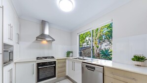 A modern kitchen with white cabinets, stainless steel appliances, and a window with a view of greenery.