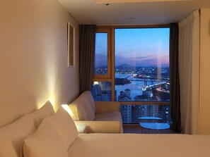 Et hotelværelse med stort vindue, sofa, lille bord og lampe.