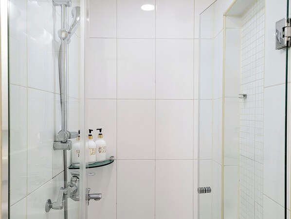 Et moderne badeværelse med en brusekabine i glas, en glashylde med toiletartikler og hvide flisevægge.