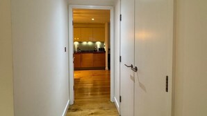 A hallway with wooden flooring leading to a kitchen area with wooden cabinets and a countertop. - A brand new apartment decorated to a  high standard in a landmark development. (London)