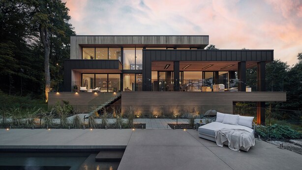 Une maison moderne dotée d’une grande façade vitrée, d’un espace extérieur spacieux avec un canapé et une petite piscine, ainsi que d’un escalier menant à un niveau supérieur.