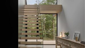 Un intérieur moderne avec un escalier en bois menant à un balcon, une console décorative et une vue sur les arbres.