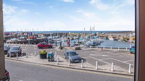 Ein Yachthafen mit vertäuten Booten, ein Parkplatz mit Autos und freie Sicht auf das Meer.