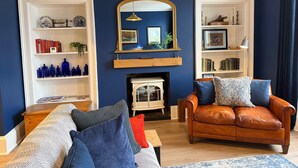 Ein Wohnzimmer mit blauer Wand, Kamin, Ledersofa, gemustertem Sofa und Bücherregalen.