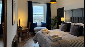 Ein Hotelzimmer mit einem großen Bett, einem Schreibtisch mit Stuhl, Blick auf die Stadt und einer Deckenleuchte.