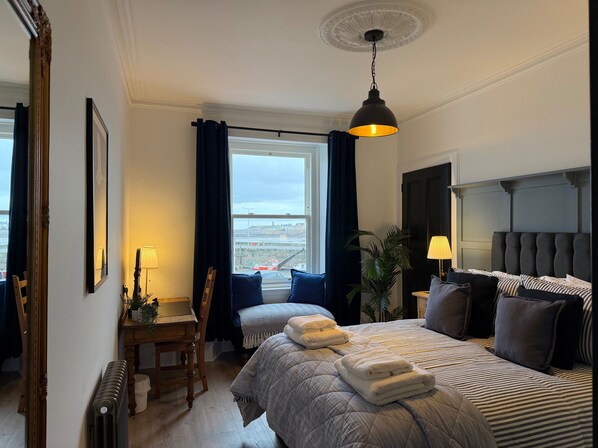 Une chambre d’hôtel avec un grand lit, un bureau avec une chaise, une vue sur la ville et un luminaire au plafond.