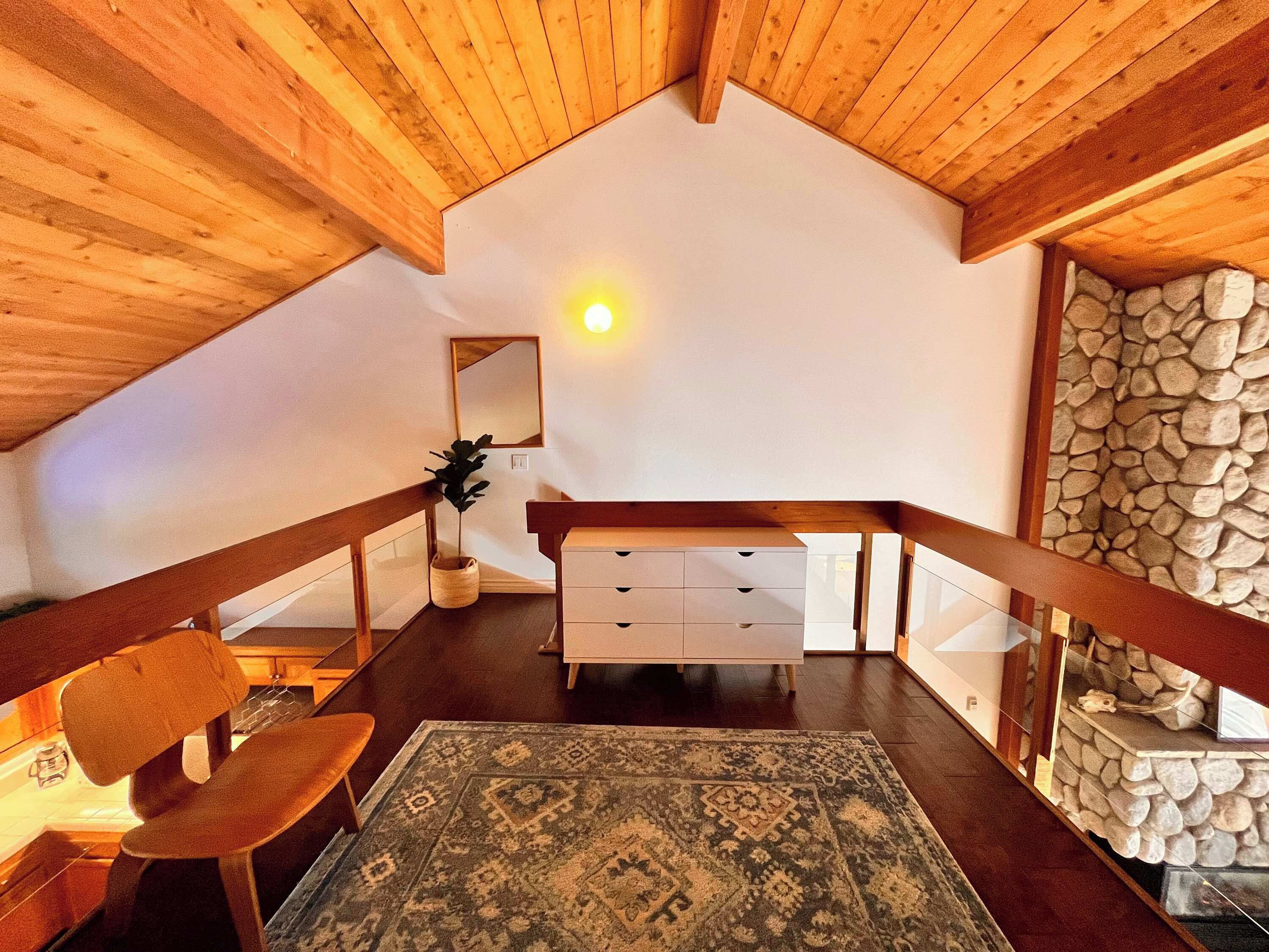 Ein gemütliches Schlafzimmer im Dachgeschoss mit Holzbalken, einer Steinwand, einem großen Spiegel und einem rustikalen Holzstuhl.