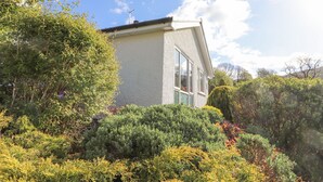 A small, single-story house with a sloped roof, surrounded by lush greenery and flowering plants. - Wansfell View (Ambleside)