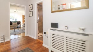 A modern living room with a sofa, a coffee table, and a rug. There is a hallway with a white console table and a mirror. - Wansfell View (Ambleside)