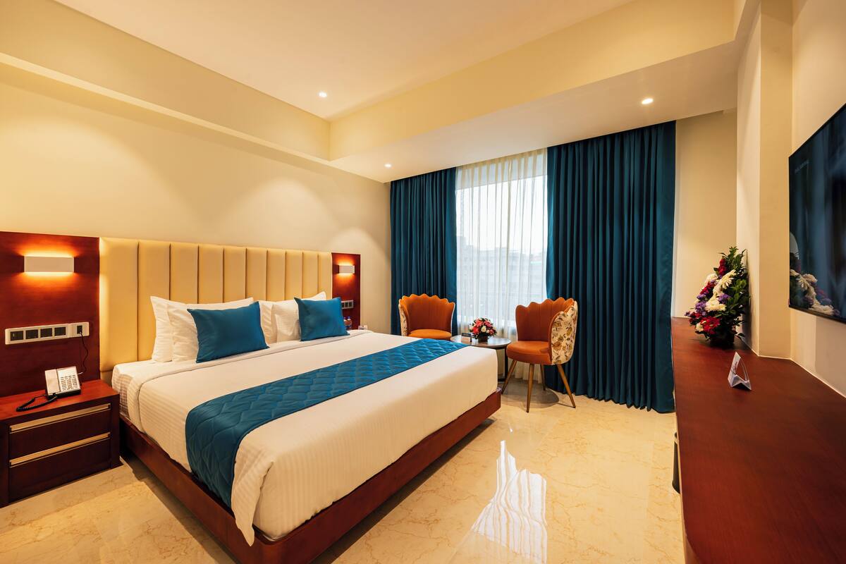 Une chambre d’hôtel avec un grand lit, une table de chevet avec un téléphone, un bureau avec une chaise, une télévision et une fenêtre avec des rideaux.