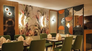 A restaurant with green chairs, a table set with plates and napkins, and a wall with a tropical mural. - Hotel Classic Pavilion (Thiruvananthapuram)