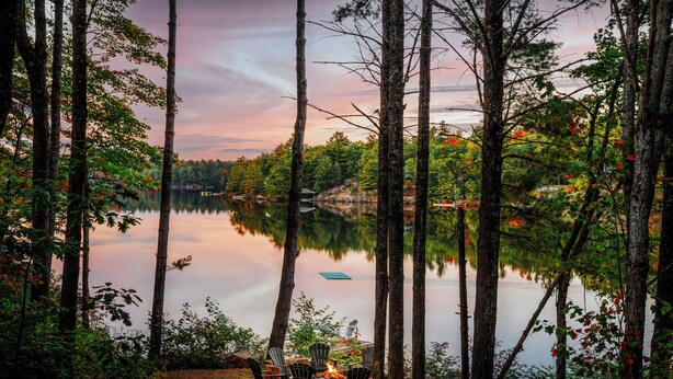 A serene lakeside setting with a fire pit and chairs, surrounded by tall trees and a calm lake. - Top Rated Muskoka - Sauna • Fireplace • Chef Kitchen (Gravenhurst)