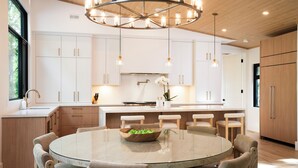 Una cocina moderna con armarios blancos, una mesa redonda de vidrio y una isla central.