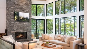 A modern living room with a stone fireplace, large windows, a sofa, and a coffee table. - Top Rated Muskoka - Sauna • Fireplace • Chef Kitchen (Gravenhurst)